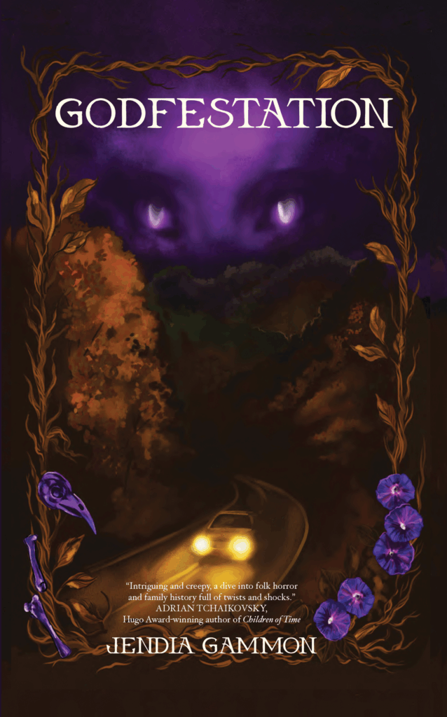 Cover art for the novella GODFESTATION written by Jendia Gammon, art by Danika Corrall. A late autumn bronze leaf and vine border frames the book, with a purple animal skull on the lower left, and purple morning glory blossoms on on the lower right. Within the frame at the top, a large, strange purple face with oddly shaped eyes looms over a dark Southern Appalachian mountain range with a mountain road, down which a car drives with its headlights on.